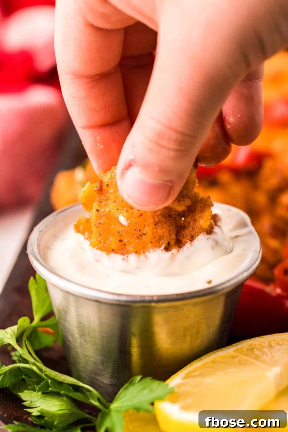 A woman's hand dipping wild west shrimp into a creamy ranch dressing, highlighting the crispy texture.