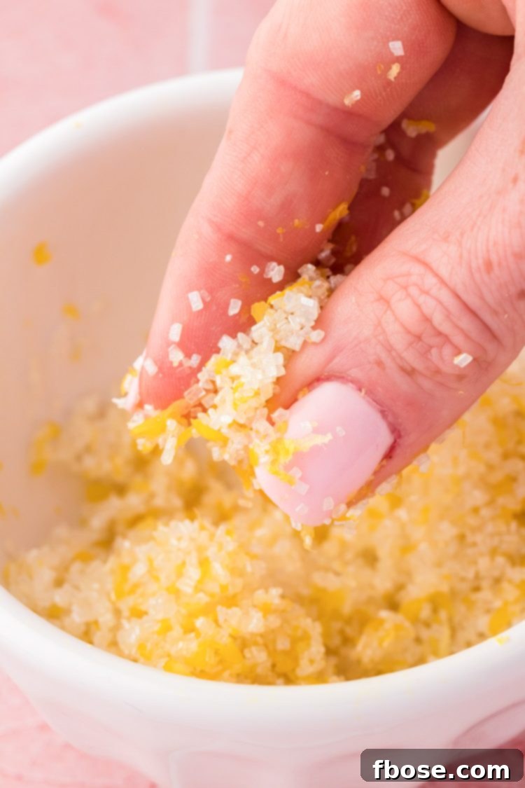 A close-up of hands rubbing coarse sparkling sugar with lemon zest in a small bowl, infusing the sugar with citrus aroma.