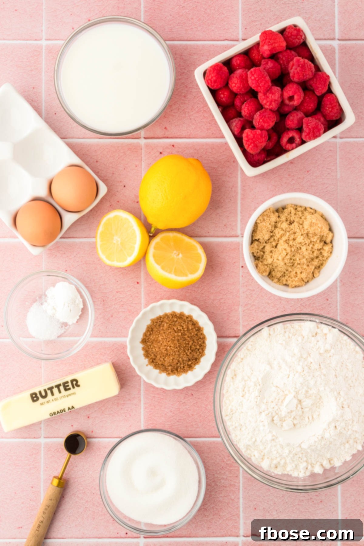 An overhead view of various ingredients meticulously prepped and arranged on a vibrant pink surface, showcasing everything needed to bake the lemon raspberry cake.
