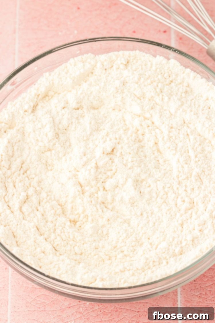A glass bowl containing whisked flour, baking powder, and salt, highlighting the prepared dry ingredients for the cake.