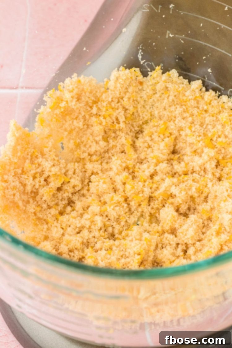 Granulated sugar and fresh lemon zest are being mixed together in a large stand mixer bowl, releasing the fragrant lemon oils.