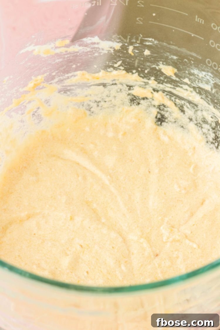Smooth, light yellow cake batter swirling in a glass mixing bowl, showcasing its creamy consistency after eggs and butter are incorporated.