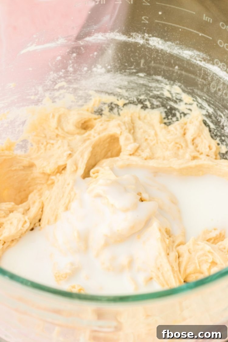 Buttermilk being poured into the cake batter, part of the alternating wet and dry ingredient addition process.
