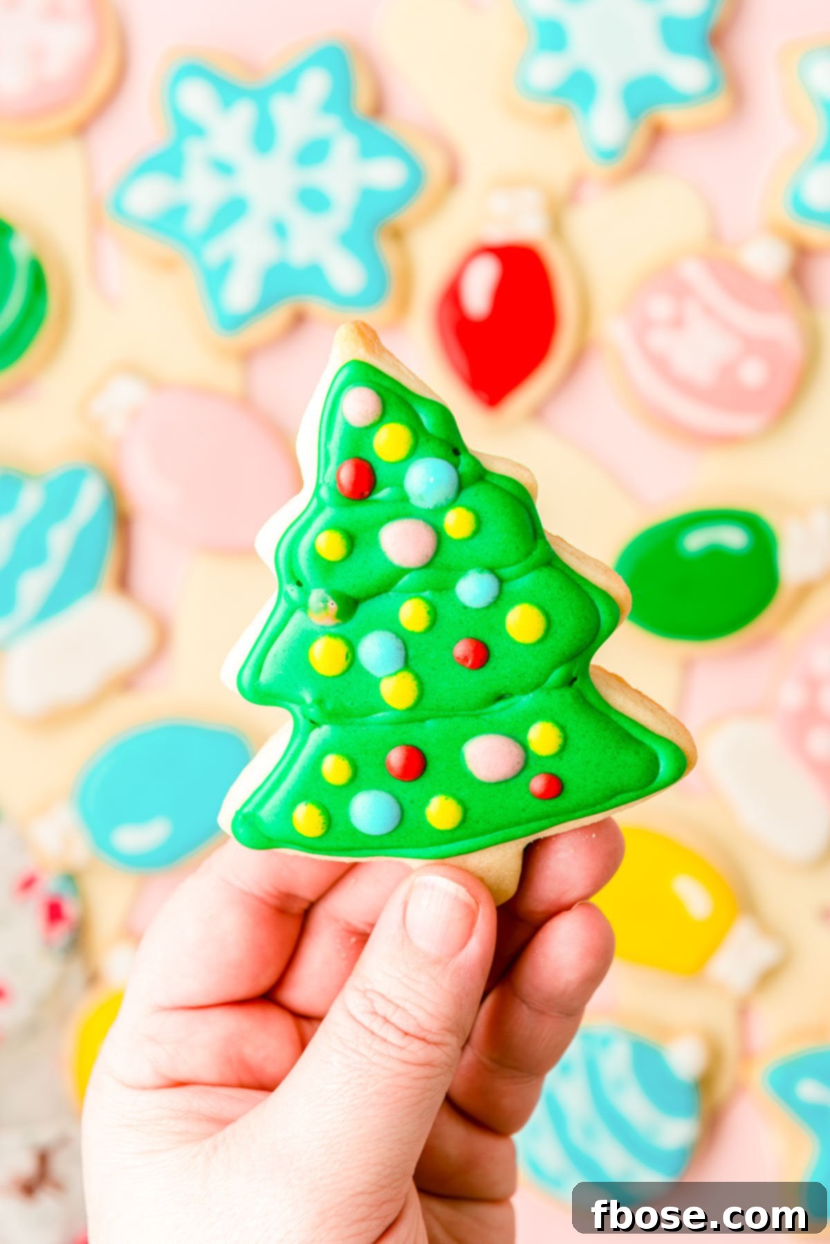 A woman's hand holing an iced Christmas tree cookie to the camera.