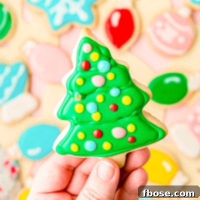 A woman's hand holing an iced Christmas tree cookie to the camera.