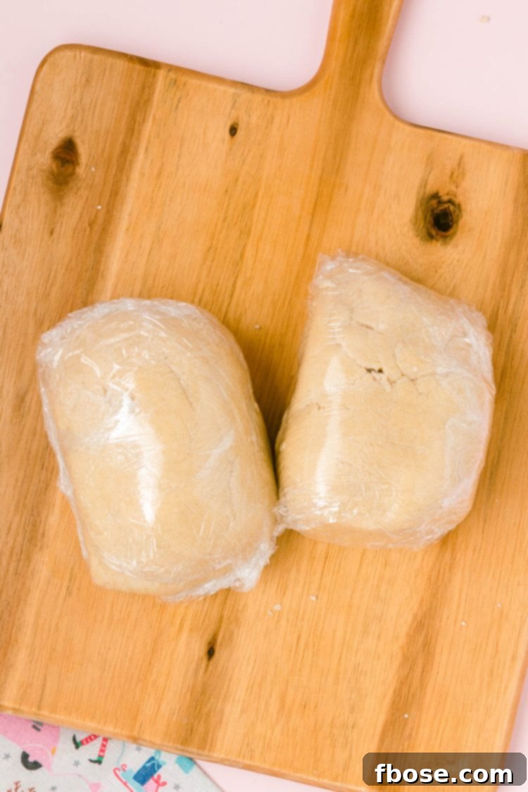 Dough divided into two portions wrapped in plastic wrap on a wooden board.