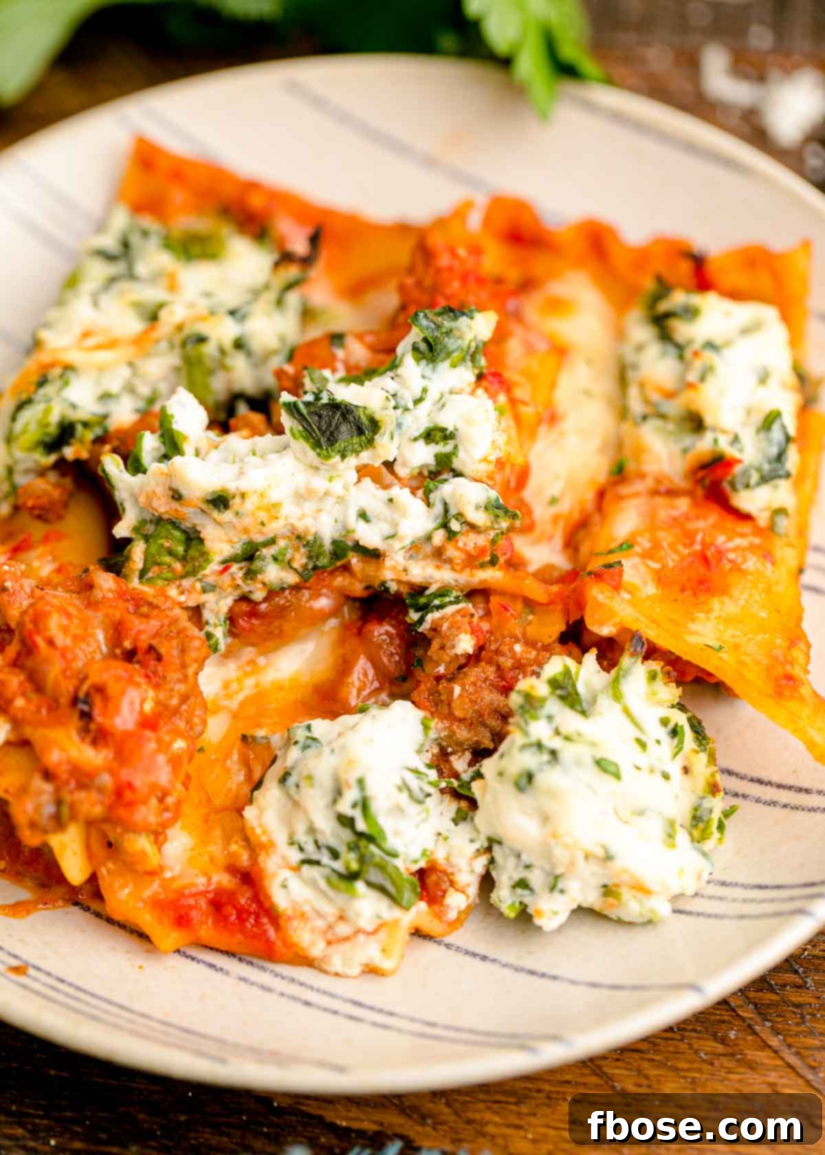 A perfectly portioned slice of sheet pan lasagna on a striped plate, highlighting the crispy edges and melty cheese.