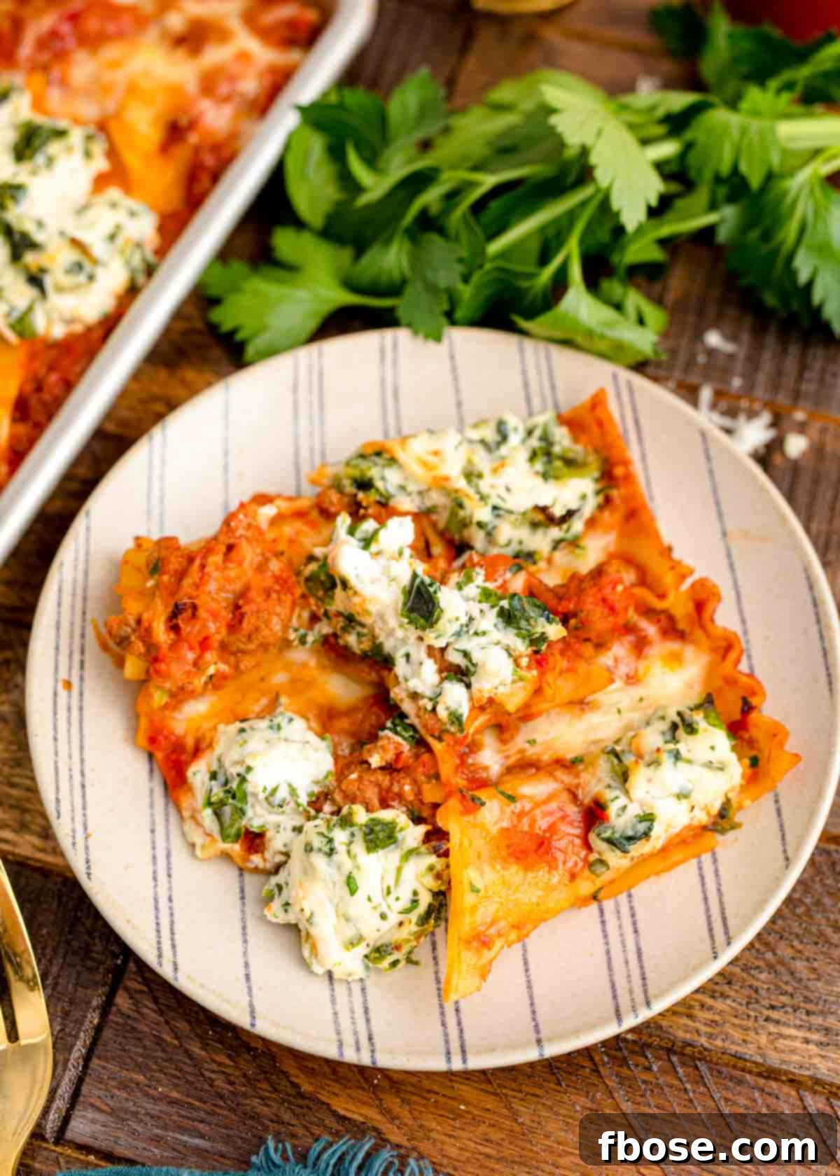 A perfectly cooked slice of sheet pan lasagna on a white striped plate, ready to be enjoyed.