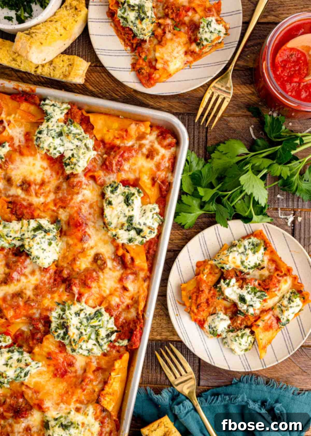 Overhead photo of a full sheet pan lasagna alongside slices on individual plates on a wooden table, invitingly served.