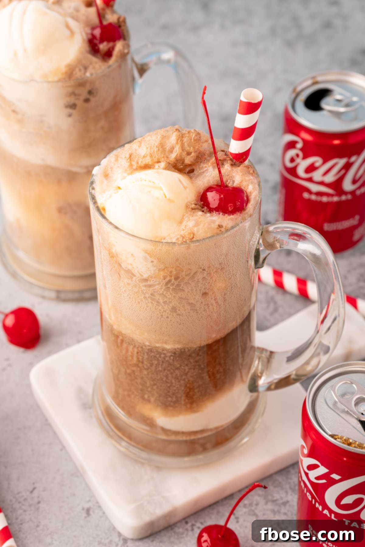 Two beer steins filled with coke floats with coke cans around them.