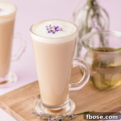 Two mugs of lavender lattes on a wooden serving board on a purple surface.