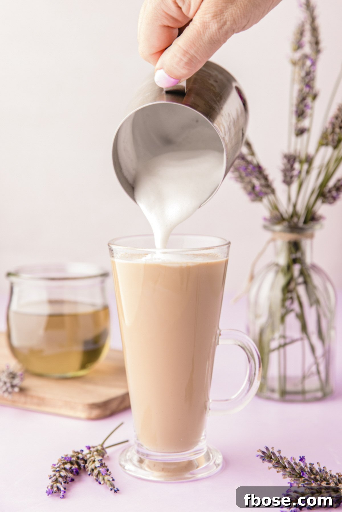 Velvety steamed milk being expertly poured into a mug already containing rich espresso and fragrant lavender syrup, creating the perfect layering for a latte.