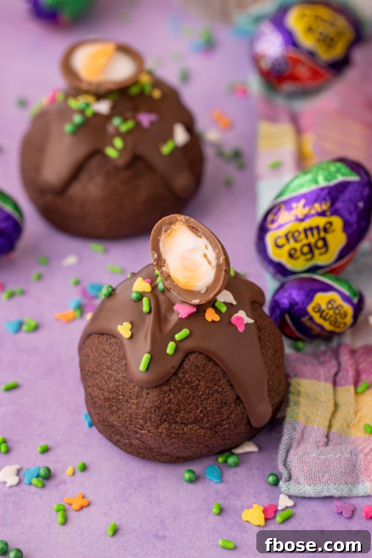 Ultimate Cadbury Creme Egg Cookies 7 A chocolate cookie topped with mini cadbury creme egg on a purple surface.