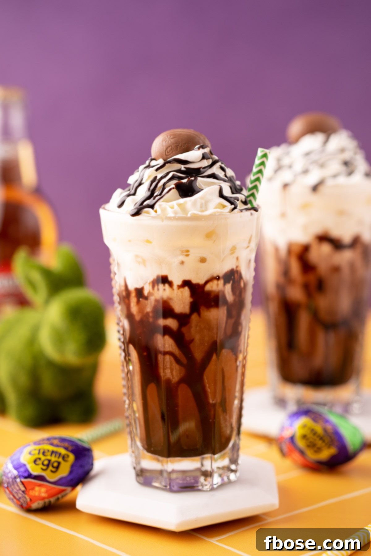 A Cadbury Creme Egg flavored dirty soda on a white coaster on a yellow table.
