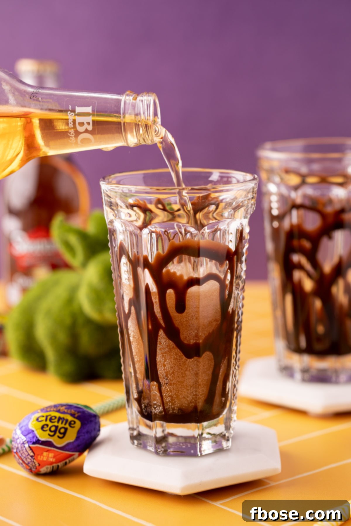 Cream soda being poured into a glass with chocolate syrup.