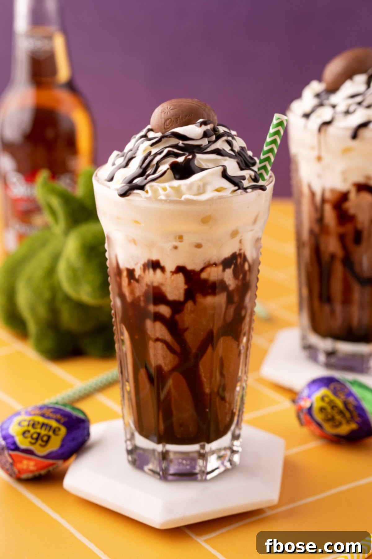 A Cadbury Creme Egg flavored dirty soda on a white coaster on a yellow table.