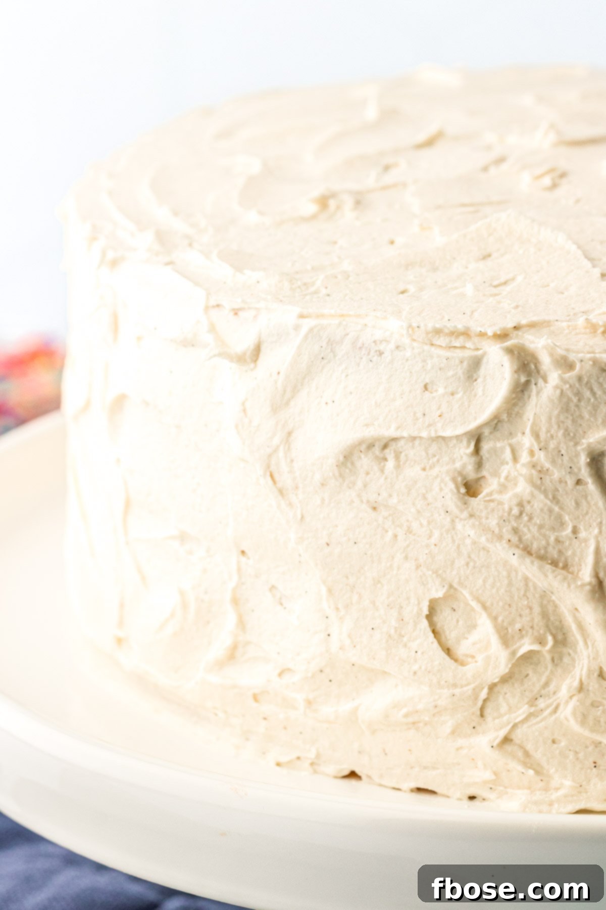 Vanilla frosted cake on a white cake stand.