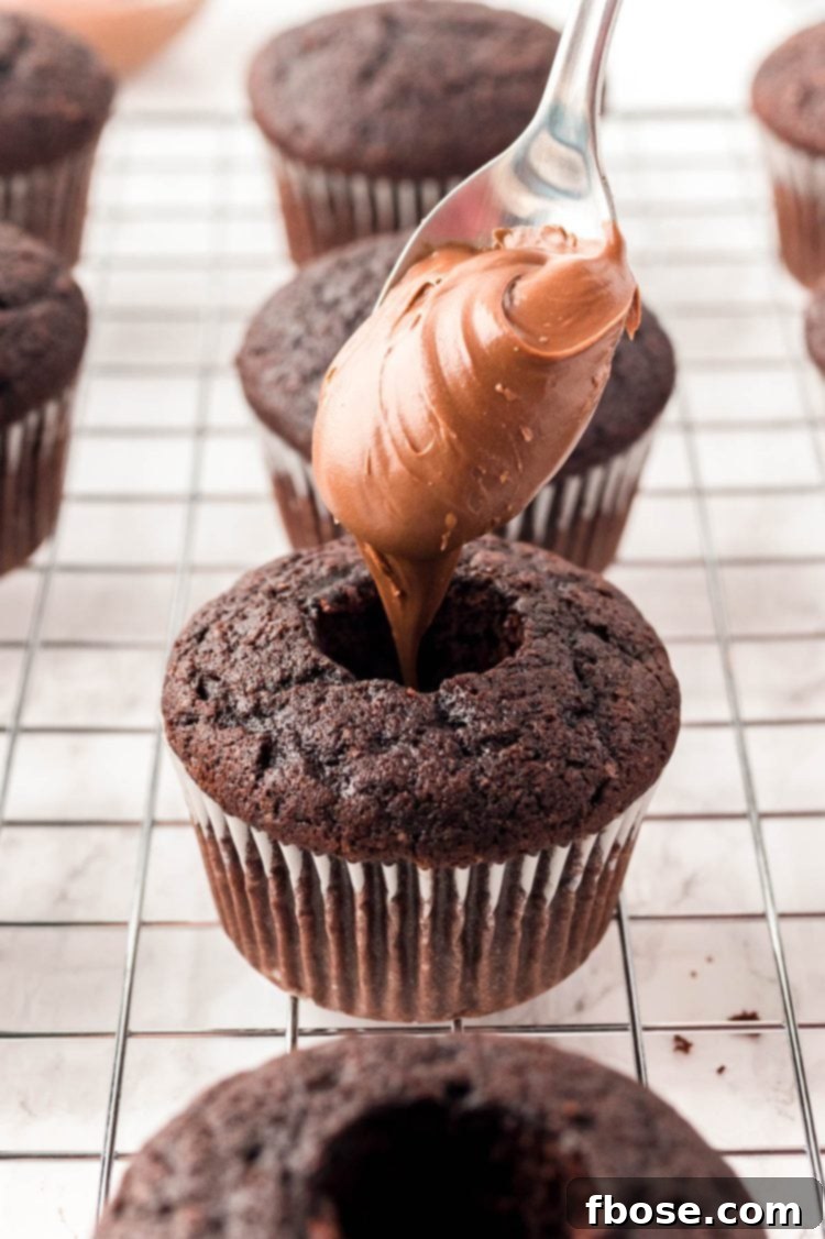 Decadent Nutella Cupcakes 6 Thick, rich Nutella being carefully spooned into the cored center of a chocolate cupcake.