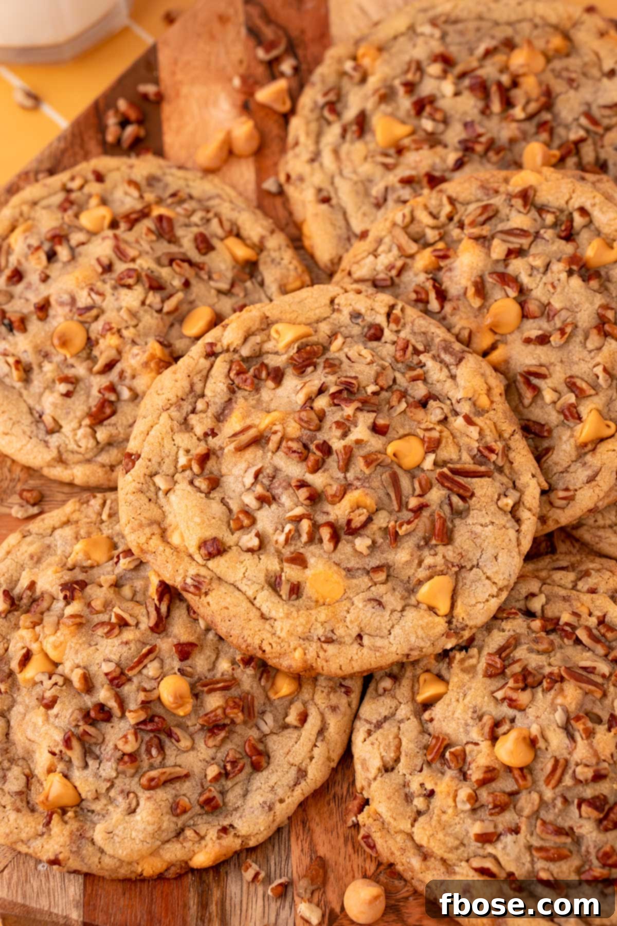 Overhead photo of golden-brown butter pecan cookies generously studded with pecans and chips, arranged on a rustic wooden serving board.