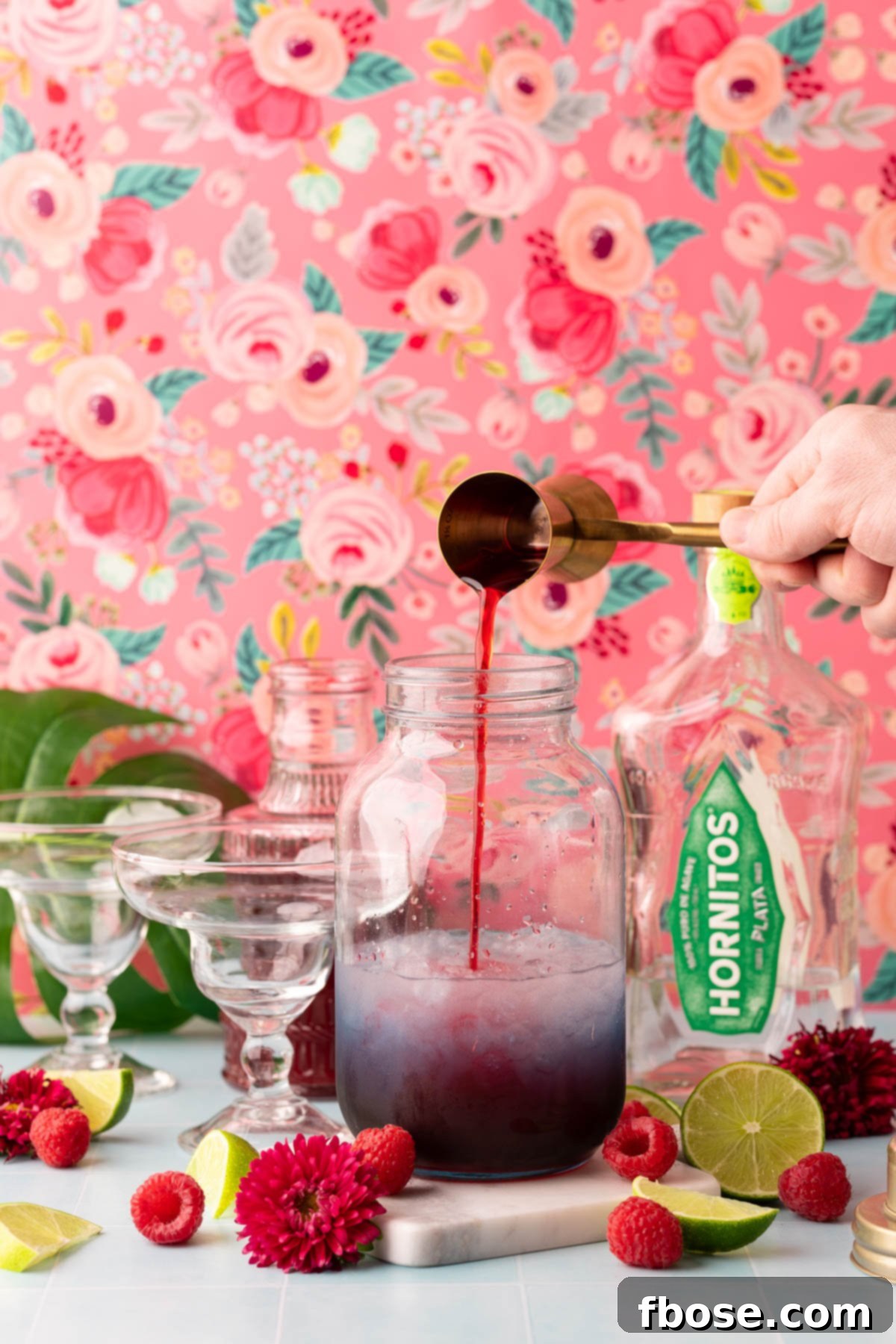 A jigger pouring raspberry simple syrup into a cocktail shaker.