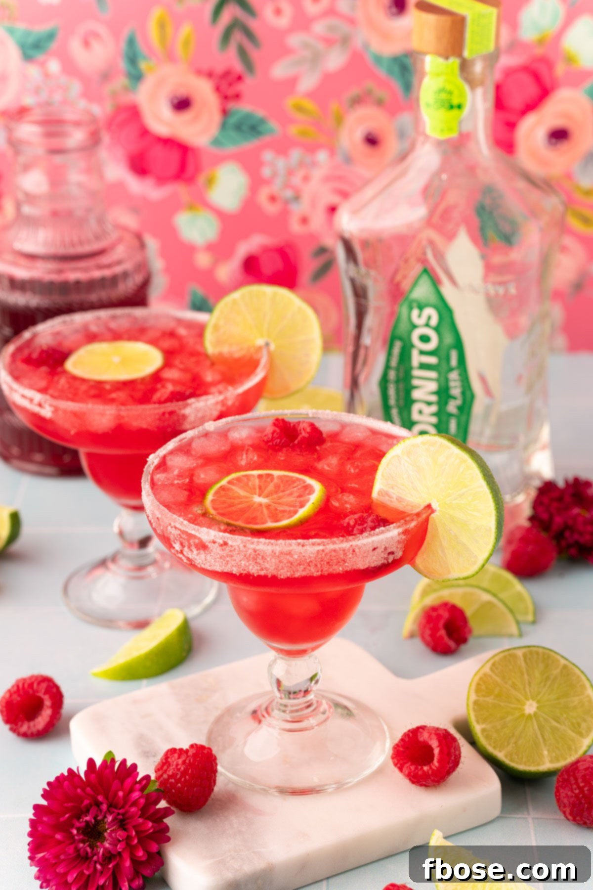 Two margarita glasses filled with raspberry margaritas on a blue table.