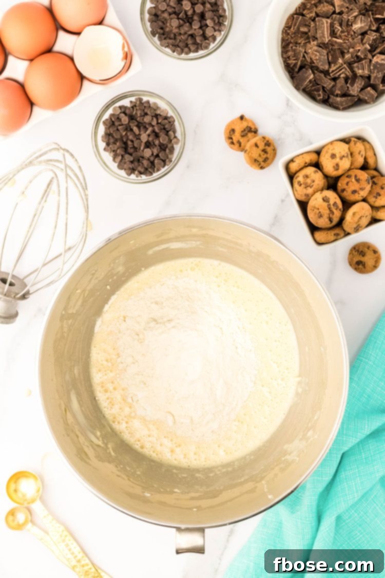 Flour being added to a stand mixer bowl with batter to make cupcakes.