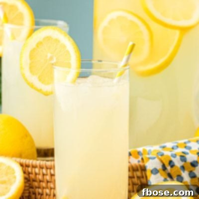 Homemade Lemonade in a glass with a pitcher behind it.