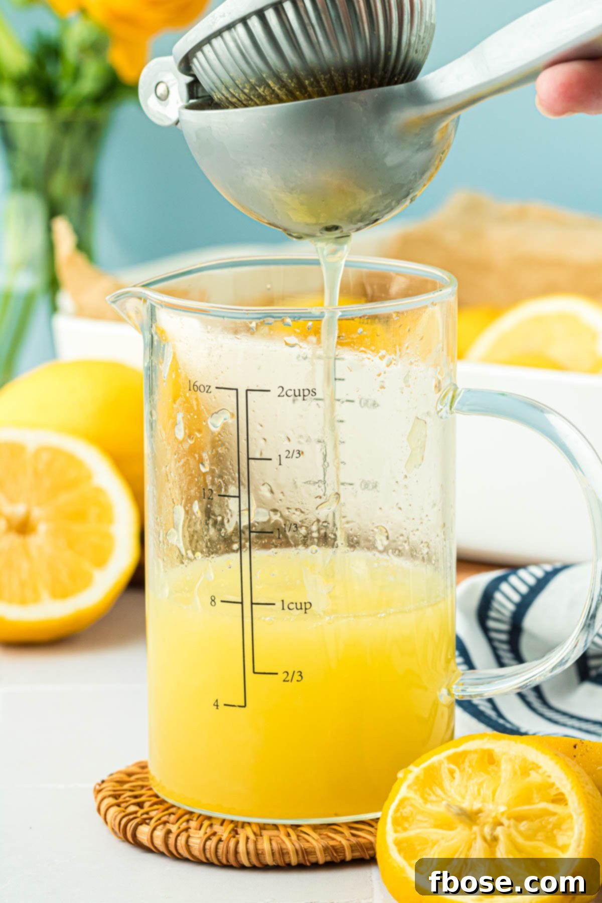 Close-up photo of lemons being pressed for juice into a liquid measuring cup using a citrus juicer.