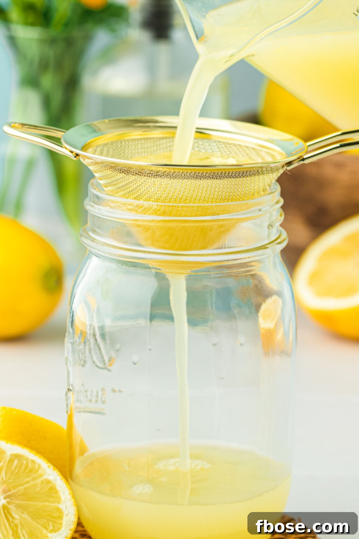 Freshly squeezed lemon juice being poured through a fine-mesh sieve into a glass bowl, catching pulp and seeds.