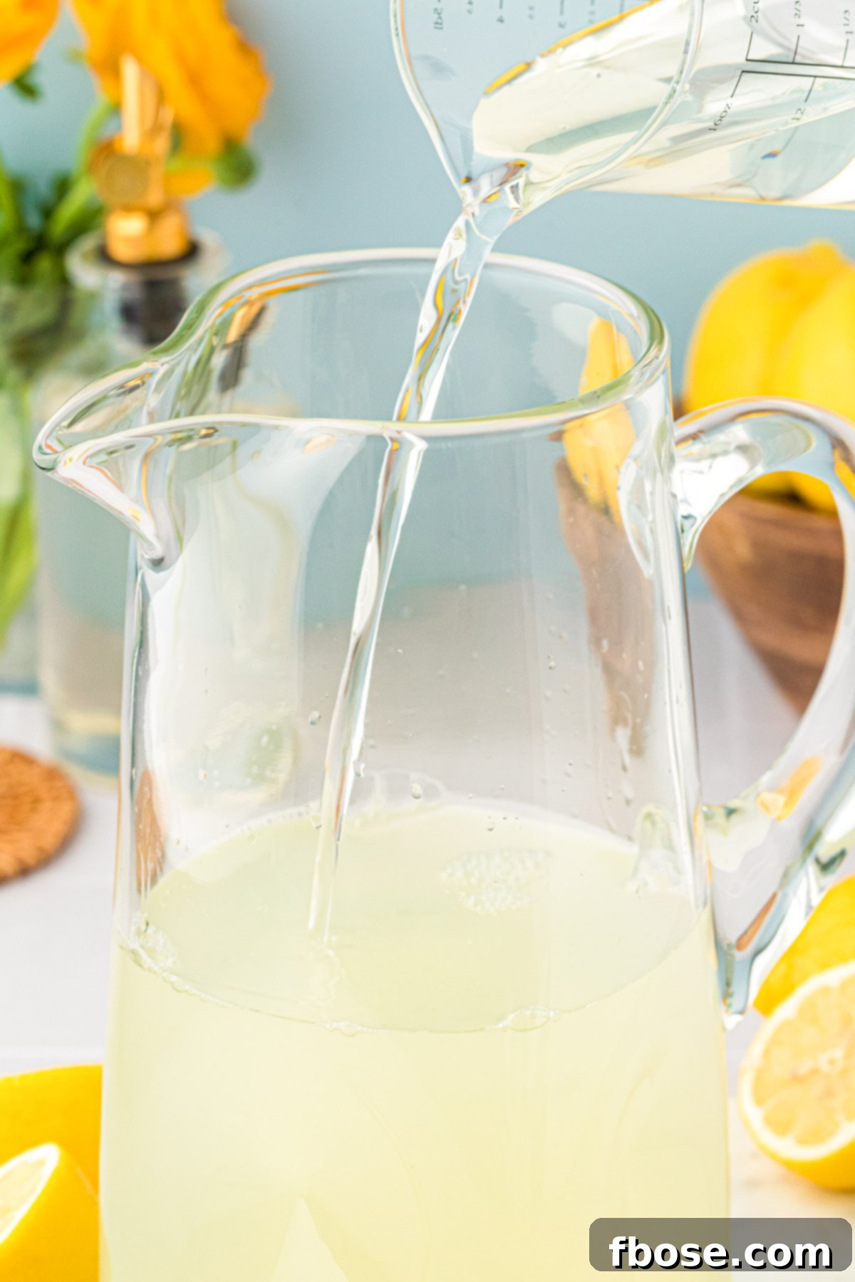Cold water being poured into a large glass pitcher containing lemon juice and simple syrup to make lemonade.