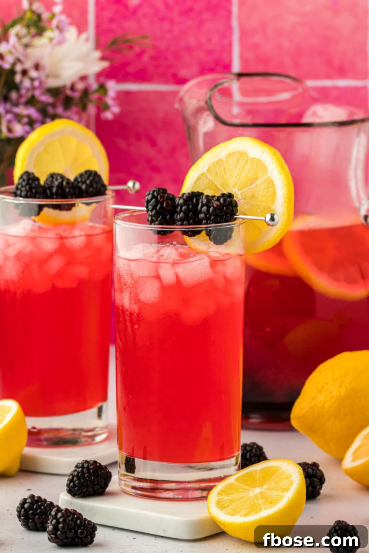Delicious Homemade Blackberry Lemonade 2 Two glasses of homemade blackberry lemonade, garnished with fresh fruit and mint, resting on a rustic counter. The vibrant purple hue of the drink stands out, promising a refreshing experience.
