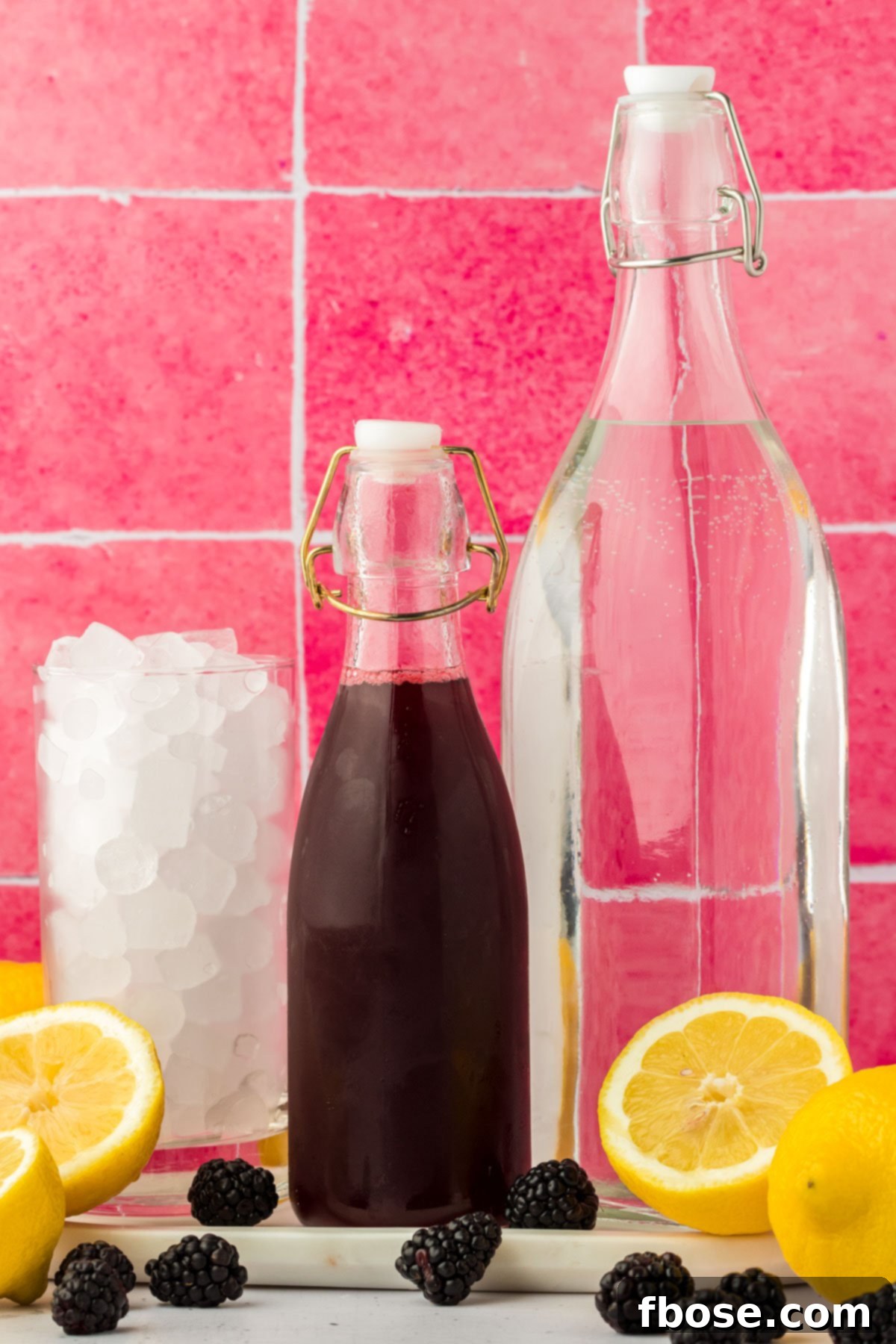 Delicious Homemade Blackberry Lemonade 4 A collection of fresh ingredients laid out on a kitchen counter, including bright yellow lemons, ripe purple blackberries, a bowl of granulated sugar, and a glass of water, all ready to make blackberry lemonade.