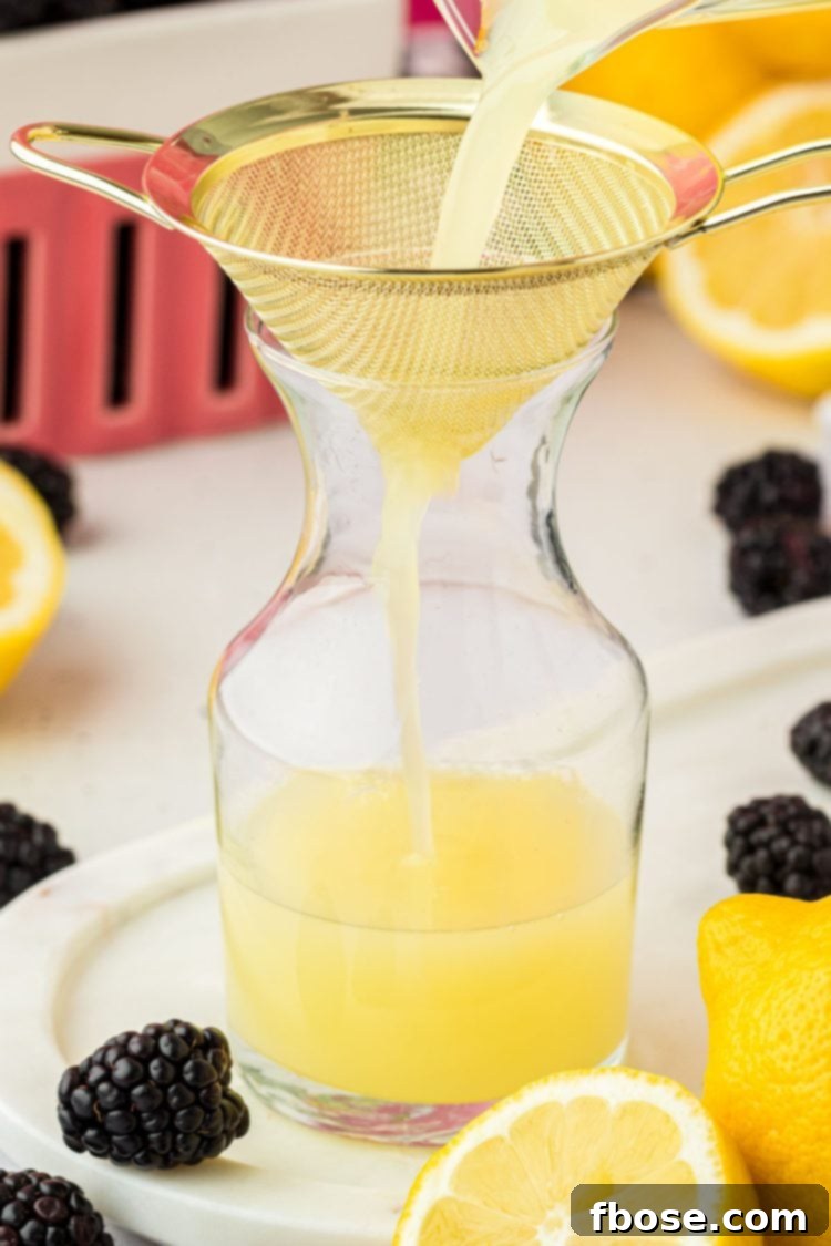 Delicious Homemade Blackberry Lemonade 7 Golden lemon juice being meticulously poured through a fine mesh sieve into a glass bottle, ensuring a smooth and clear liquid.
