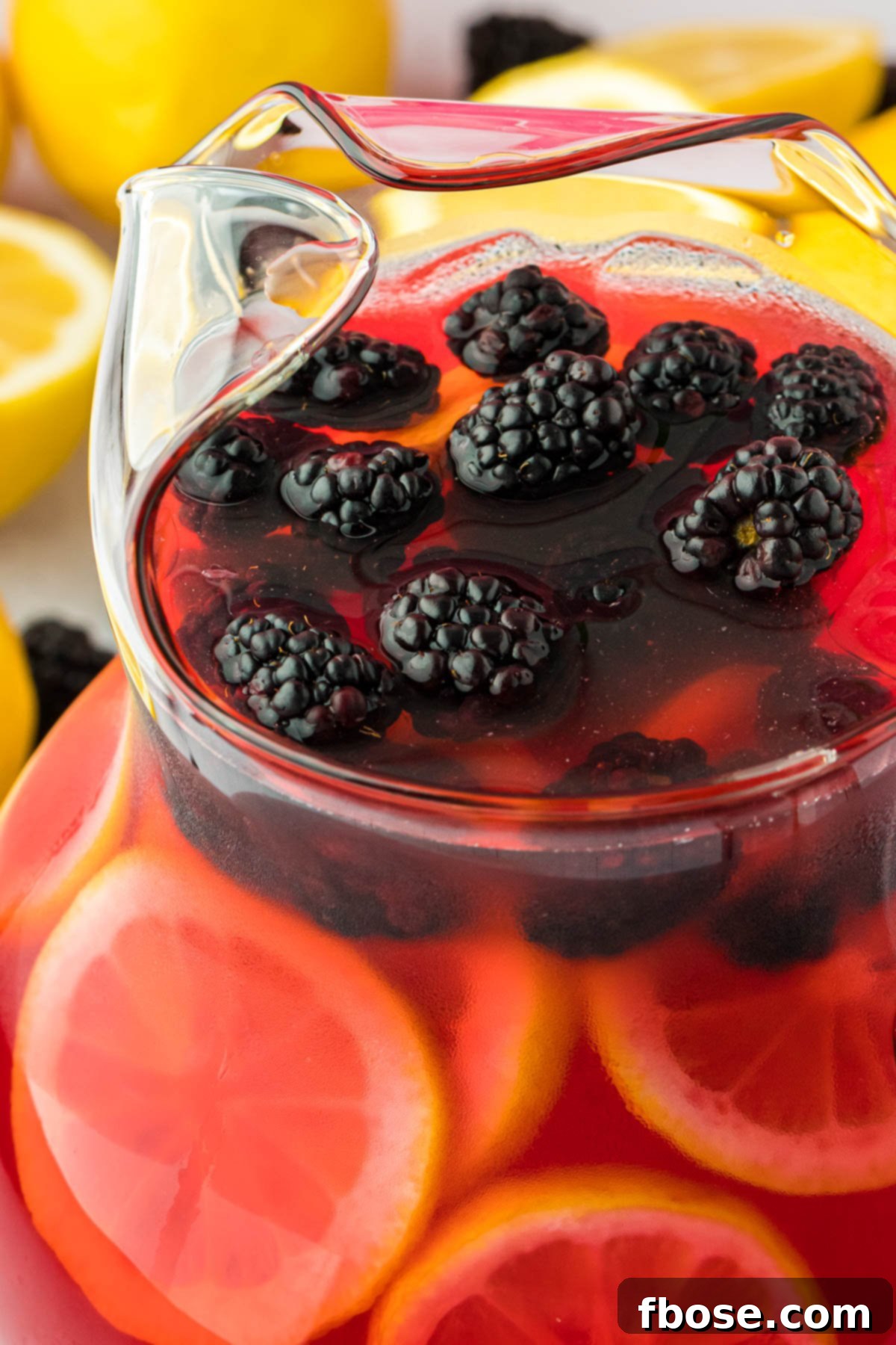 Delicious Homemade Blackberry Lemonade 9 A large glass pitcher filled with vibrant blackberry lemonade, garnished with fresh lemon slices, ready to be served. Its refreshing color stands out on a clean backdrop.