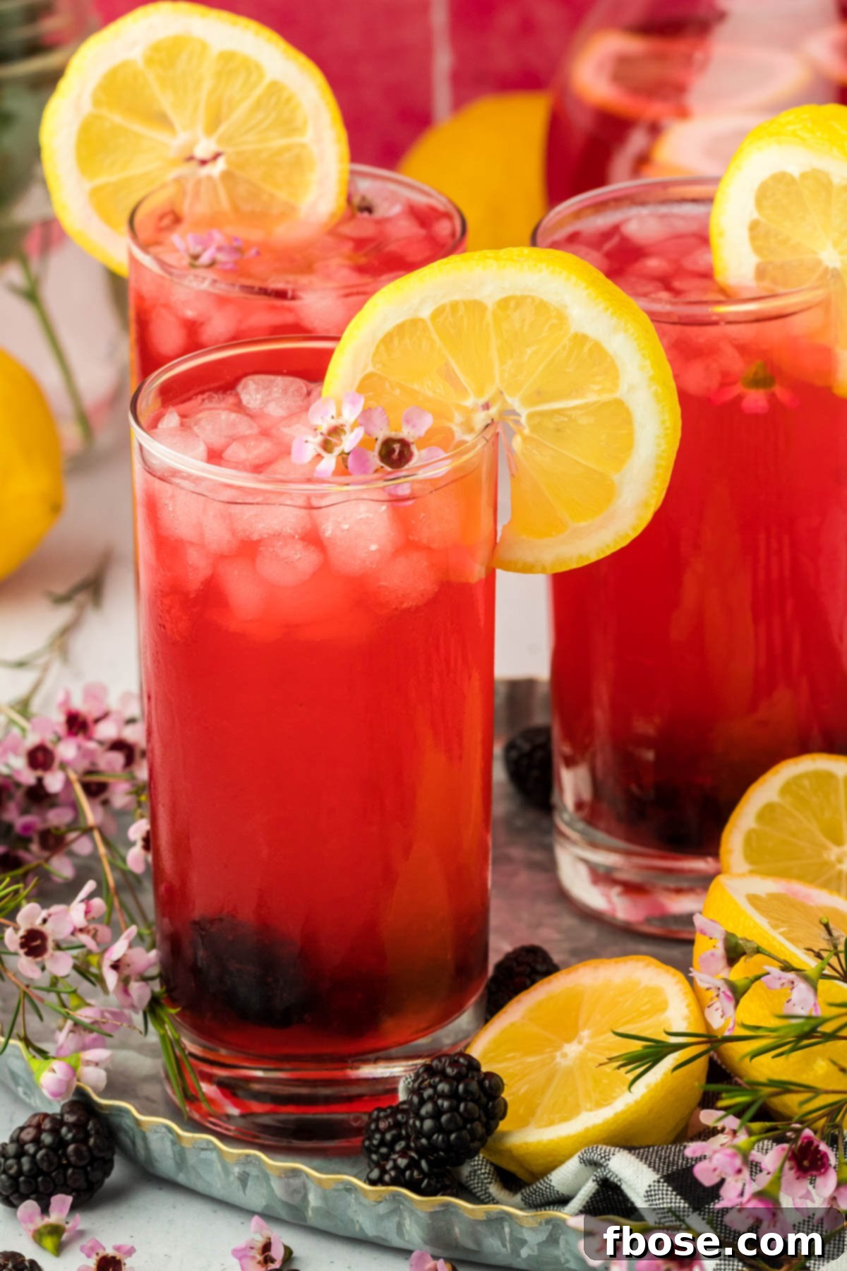 Delicious Homemade Blackberry Lemonade 10 Multiple glasses of vibrant blackberry lemonade, each garnished with fresh lemon slices and blackberries, are arranged on a rustic wooden table, creating an inviting summer scene.
