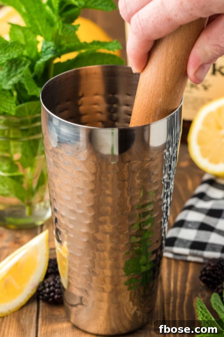 Fresh mint being muddled with a lemon wedge in a cocktail shaker.