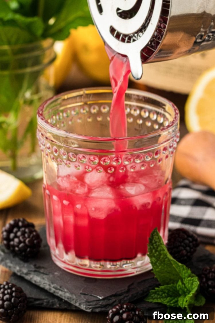 A blackberry bourbon smash being poured into a glass from a cocktail shaker.