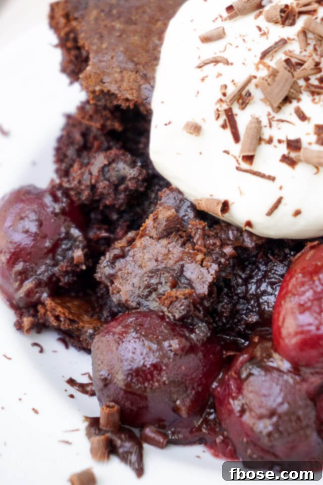 Midnight Cherry Bake 6 A generous slice of Black Forest Cobbler served on a white plate, topped with a large swirl of whipped cream and finely grated chocolate.