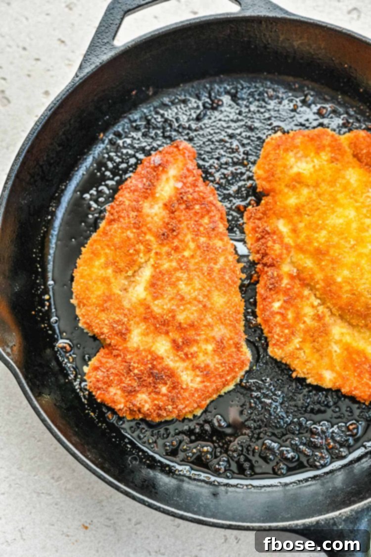 Panko crusted chicken pieces sizzling and browning in a hot skillet on the stovetop.