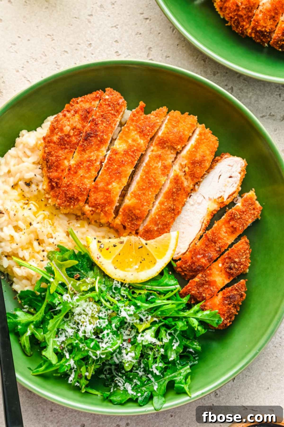 Overhead photo of perfectly cooked panko breaded chicken in a vibrant green bowl, accompanied by rice and fresh greens, ready to be served.