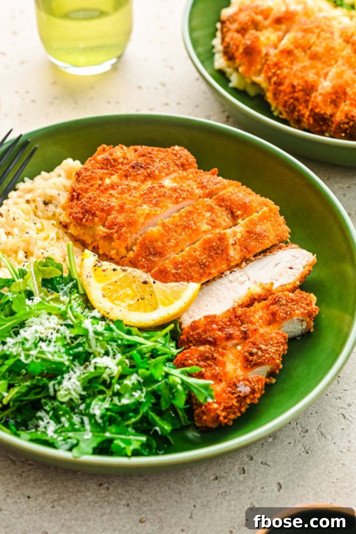 Close-up of golden-crisp panko crusted chicken pieces, served in a vibrant green bowl with rice and fresh greens.
