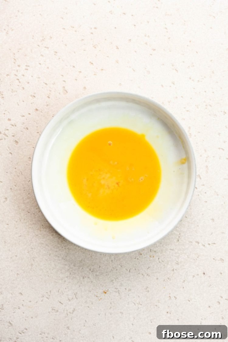 Beaten eggs in a small white ceramic bowl, ready for dipping.