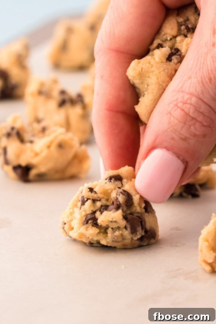 A woman's hand portioning out cookie dough on a parchment lined cookie sheet.