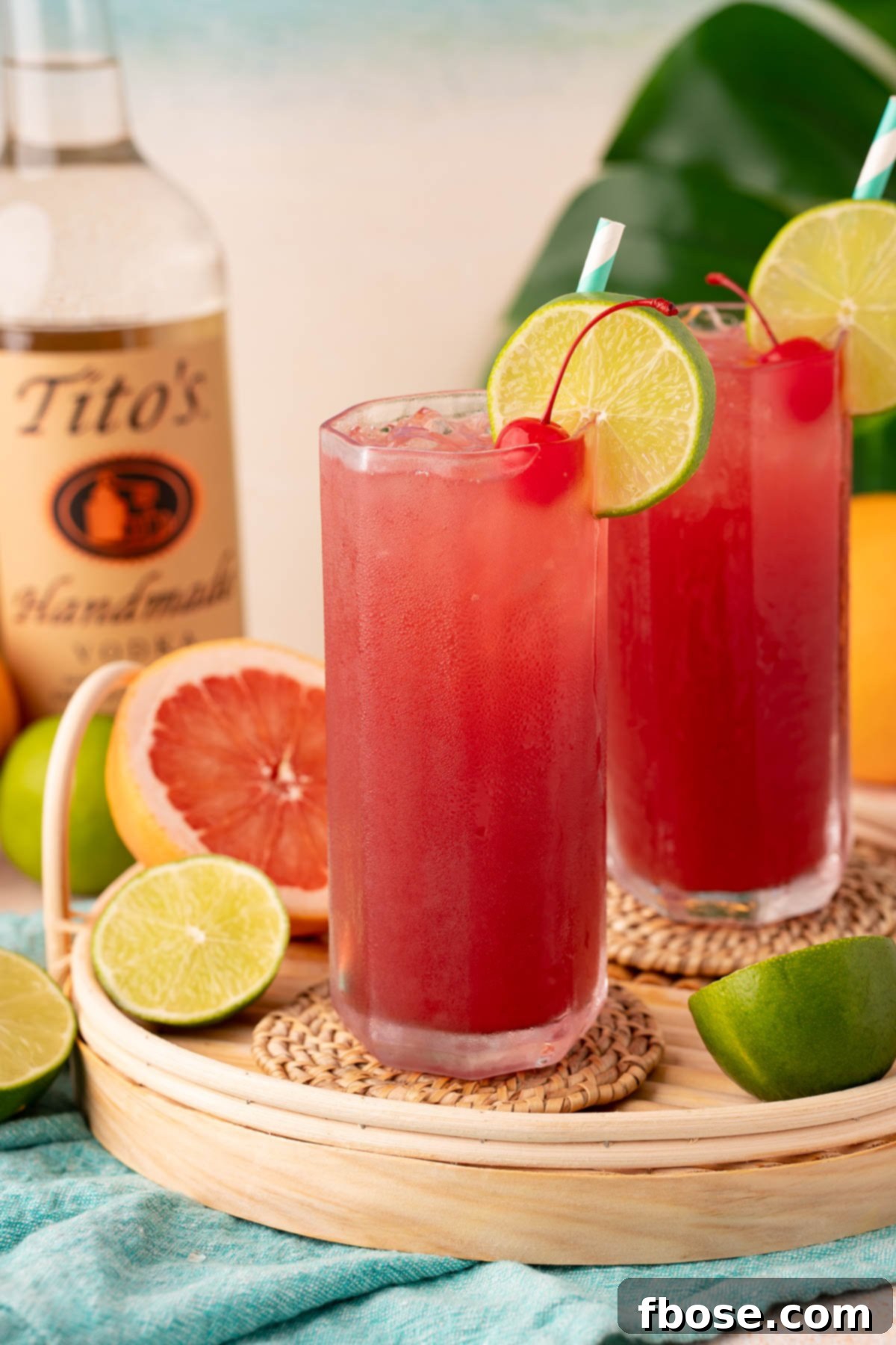 The Ultimate Sea Breeze Cocktail 2 Two vibrant Sea Breeze cocktails, garnished with lime wedges, on a rustic rattan serving tray, set against a bright backdrop.