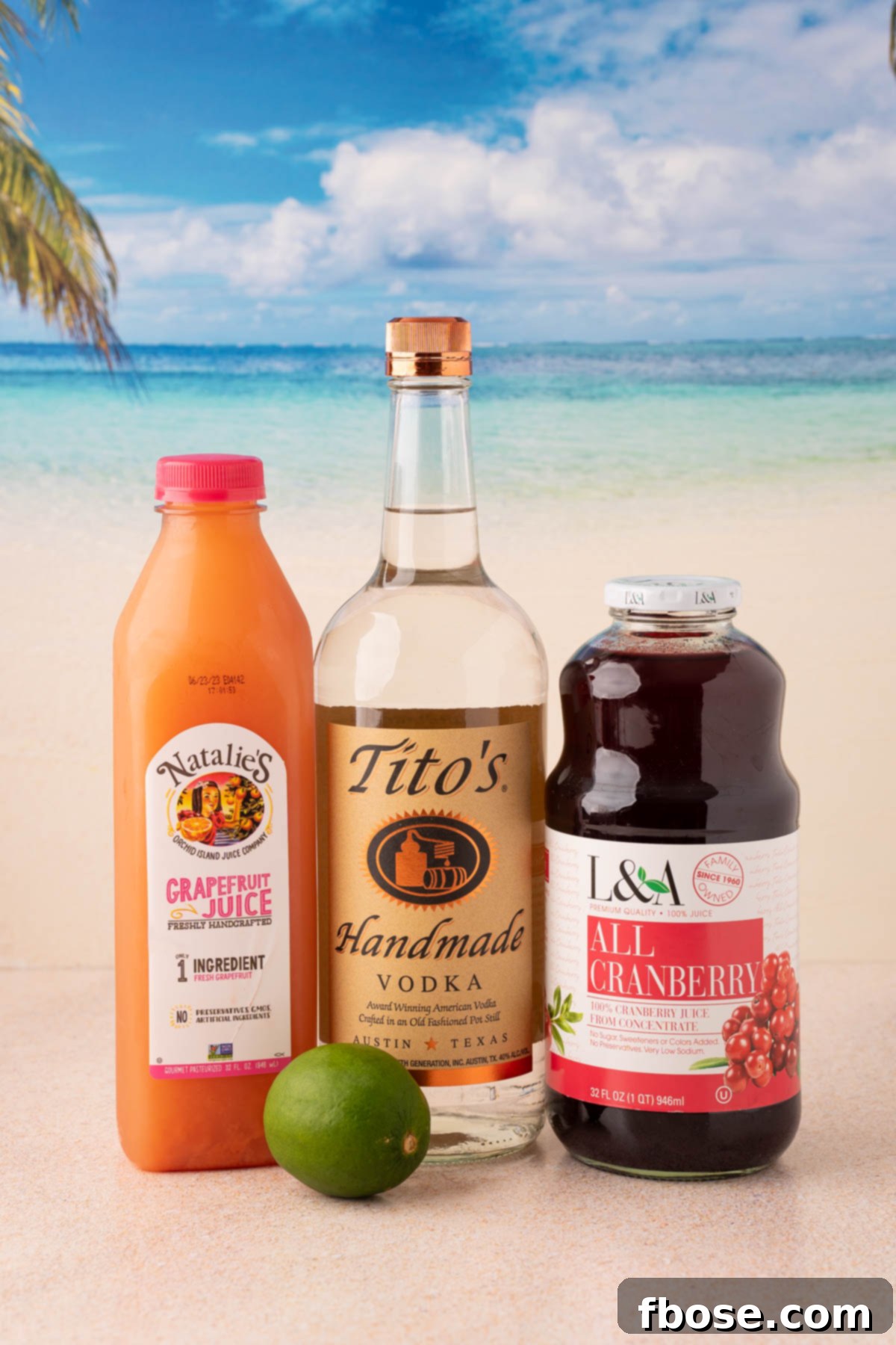 The Ultimate Sea Breeze Cocktail 4 Bottles of cranberry juice, grapefruit juice, and vodka arranged on a wooden table, alongside fresh lime slices, ready for cocktail preparation.