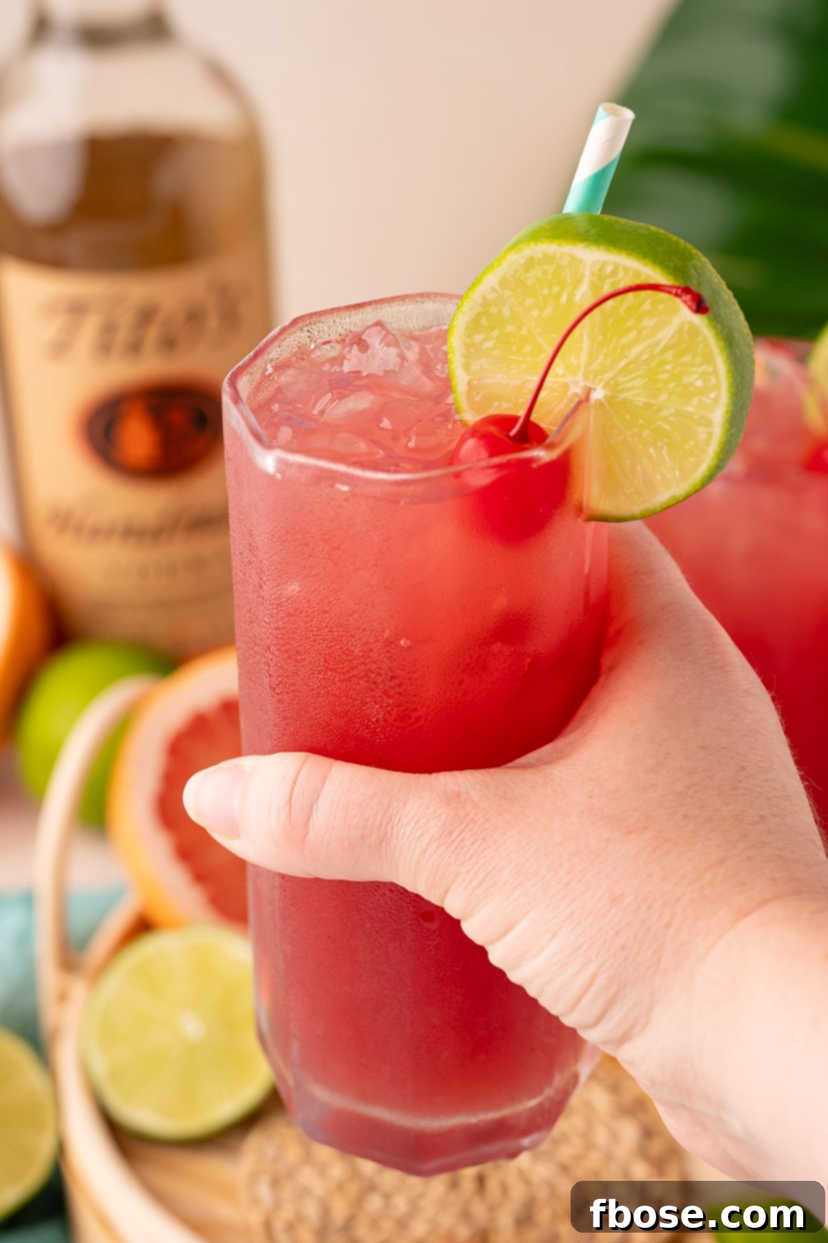 The Ultimate Sea Breeze Cocktail 5 A woman's hand extends a glass of Sea Breeze cocktail towards the camera, showcasing the vibrant drink against a soft background.