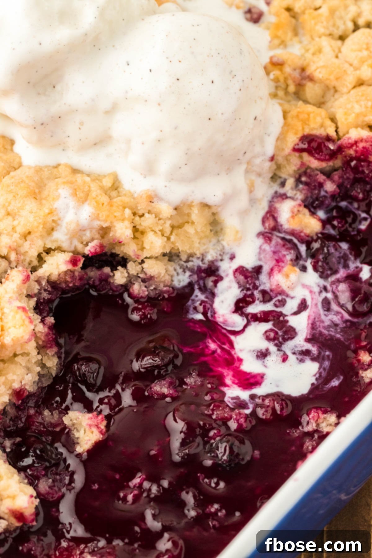 A pan filled with blueberry cobbler, vanilla ice cream melting into it.