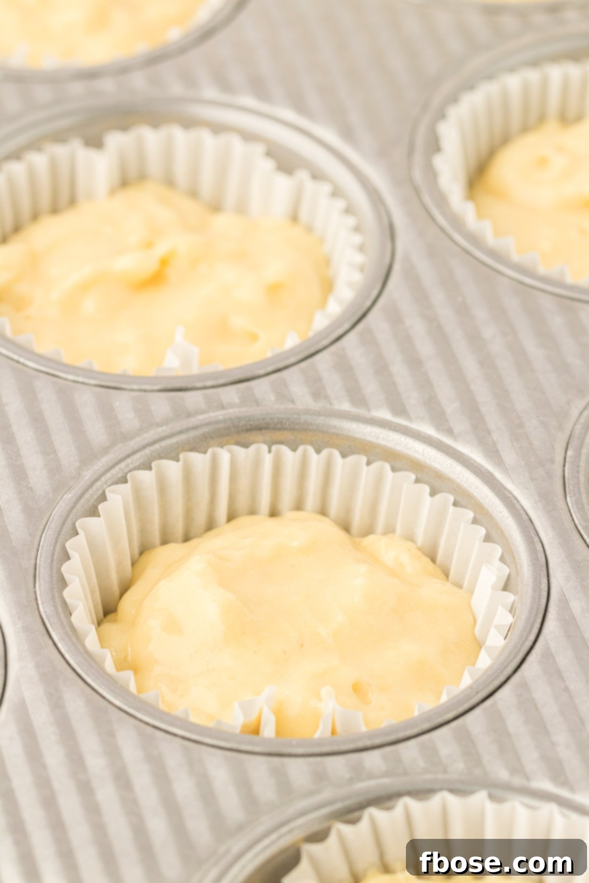 Yellow cupcake batter meticulously placed into a cupcake pan, ready for baking.