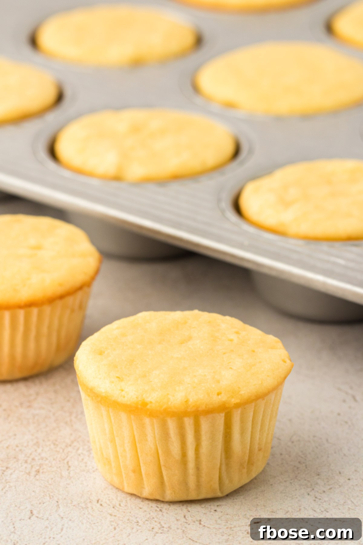 A cluster of golden yellow cupcakes cooling in a baking pan, with more alongside it.