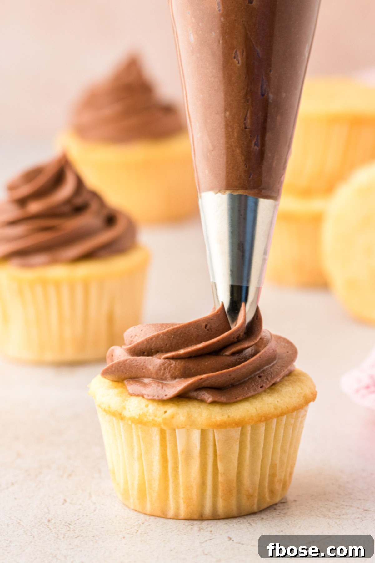 Chocolate cream cheese frosting being expertly piped onto a golden yellow cupcake.